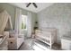 Light-filled Bedroom with a white crib, accent wallpaper, plush armchair, and soft green walls at 20510 W White Rock Rd, Buckeye, AZ 85396