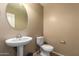 Well-lit half bathroom with a pedestal sink, toilet, and stylish round mirror at 23613 W Mobile Ln, Buckeye, AZ 85326