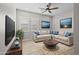 Bright living room features an L-shaped couch, a ceiling fan and large windows with shutters at 23036 E Oriole Way, Queen Creek, AZ 85142