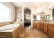 Well-lit main bathroom with a large soaking tub, wood cabinets, tile floor and an archway to the main bedroom at 35108 N 139Th Way, Scottsdale, AZ 85262