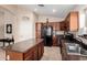 Galley kitchen with wooden cabinetry, black appliances, an island, and neutral countertops at 41847 W Sparks Ct, Maricopa, AZ 85138