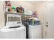 Functional laundry room with white washer and dryer units, storage shelves, and a closed door at 41847 W Sparks Ct, Maricopa, AZ 85138