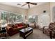 Comfortable living room featuring a brown sofa, ceiling fan, and natural light from the large window at 41847 W Sparks Ct, Maricopa, AZ 85138
