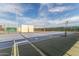 Outdoor tennis court with blue and green surface, nets, fencing, and stadium lights under a bright sky at 10724 W Cheryl Dr, Sun City, AZ 85351