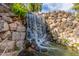 Scenic community waterfall feature over decorative stone landscaping with lush green plants and running water at 10724 W Cheryl Dr, Sun City, AZ 85351