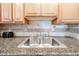 Close-up showcasing a kitchen sink area with granite countertops, wooden cabinetry, and tile backsplash at 10827 W Santa Fe Dr, Sun City, AZ 85351