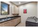 Well-lit laundry room includes cabinets, dark countertops, stainless sink, modern washer and dryer, and view of desert landscape at 39602 N Charles Blair Macdonald Rd, Scottsdale, AZ 85262