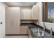 Bright laundry room featuring light wood cabinets, black granite countertops, and a stainless steel sink at 39602 N Charles Blair Macdonald Rd, Scottsdale, AZ 85262