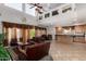 Bright living room featuring high ceilings, a leather sofa, and an open layout to the kitchen and dining area at 43228 W Knauss Dr, Maricopa, AZ 85138