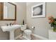 Stylish powder room with a pedestal sink, decorative mirror, neutral walls, and elegant flower artwork at 5291 S Bradshaw Pl, Chandler, AZ 85249