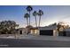 Contemporary home showcasing clean lines, dark wood garage doors, minimalist landscaping, and towering palm trees at dusk at 23002 N Country Club Trl, Scottsdale, AZ 85255