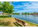 Scenic view of a tranquil community pond featuring a central fountain, lush trees, grassy banks, and a relaxing park bench at 43615 W Roth Rd, Maricopa, AZ 85138