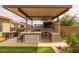 Covered outdoor kitchen with grill, mini-fridge, bar seating, television, and stone accents, perfect for entertaining at 5250 S Wesley Cir, Mesa, AZ 85212