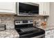 Close-up of stainless steel oven and microwave with granite countertops and mosaic backsplash at 16514 W Sandia Park Dr, Surprise, AZ 85374