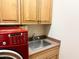 Functional laundry area includes a stainless steel sink, built-in cabinets, and a modern red washer and dryer set at 42023 N Bridlewood Way, Anthem, AZ 85086