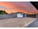 Spacious backyard with white shed, block wall, gravel and metal driveway entrance under colorful evening sky at 9005 W Villa Chula St, Peoria, AZ 85383