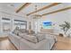 Open living room with exposed beams, large windows, a sectional sofa, and a media cabinet with mounted TV at 10006 E Rotation Dr, Mesa, AZ 85212