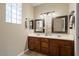 Bathroom features a double sink vanity with wood cabinets, and two framed mirrors at 11025 E Nichols Ave, Mesa, AZ 85209