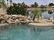 Close-up of the pool's rock waterfall feature and lush landscaping overlooking a lake at 7724 W Topeka W Dr, Glendale, AZ 85308