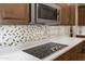 Close-up of a modern cooktop and mosaic backsplash, complemented by white quartz countertops and custom cabinets at 12516 W Mclellan Ct, Glendale, AZ 85307