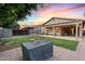 Spacious backyard featuring a covered patio, lush green lawn, storage and a beautiful sunset backdrop at 41138 N Soap Berry St, Queen Creek, AZ 85140