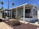 Charming mobile home with covered porch, manicured landscape, and palm trees against a vibrant blue sky at 1226 S Seneca Dr, Apache Junction, AZ 85119