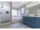 Bright bathroom featuring separate tub and shower, double sinks with blue cabinets, and window with white blinds at 29891 N Desert Angel Dr, San Tan Valley, AZ 85143