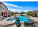 An eye-level shot of a blue, rock-lined backyard pool with an elevated jacuzzi and lounging area at 7342 E Norwood St, Mesa, AZ 85207