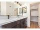 Bathroom vanity featuring double sinks, large mirrors, dark wood cabinets, and an open doorway to a walk-in closet at 2027 S Rowen St, Mesa, AZ 85209