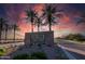 Elegant Tartesso entrance featuring lush landscaping and palm trees silhouetted against a vibrant sunset sky at 30963 W Columbus Ave, Buckeye, AZ 85396