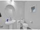 Clean half-bathroom featuring a pedestal sink, toilet, and a large, round mirror at 36085 W Prado St, Maricopa, AZ 85138