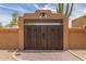 Stunning front gate in Arizona features a tan stucco wall, rustic wooden doors, and a charming bell detail at 8255 E Yearling Rd, Scottsdale, AZ 85255