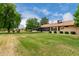 View of backyard with green grass, mature trees, and the back of the house at 13015 W Blue Sky Dr, Sun City West, AZ 85375