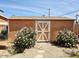 Backyard storage shed with white painted doors flanked by flowering bushes and gravel ground cover at 2027 N 81St St, Scottsdale, AZ 85257