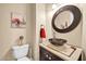 A modern half bathroom with a unique round mirror, dark vanity, and an artistic painting on the wall at 2959 W Eastman Dr, Anthem, AZ 85086