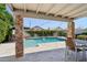 Inviting backyard oasis featuring a refreshing pool, covered patio with stone pillars, and lush landscaping at 1057 W Laurel Ave, Gilbert, AZ 85233