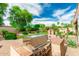 Green backyard oasis with built in gas grill, desert landscaping, mature trees, and brick paved patio at 13204 W Palo Verde Dr, Litchfield Park, AZ 85340