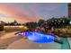 Inviting backyard pool area with lush landscaping, waterfall feature, and elegant brickwork, all set against a vibrant sunset at 6971 W El Cortez Pl, Peoria, AZ 85383