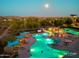 Aerial view of the community pool area, illuminated at twilight, with lush landscaping and mountain views in the background at 11872 W Duane Ln, Peoria, AZ 85383