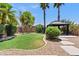 Lush backyard featuring green lawn, palm trees, rock landscaping, and a gazebo at 973 E Kelsi Ave, San Tan Valley, AZ 85140