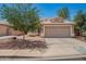 A single-story home with a well-manicured lawn and a shade tree in the front yard adds curb appeal to this tan home at 13241 W Desert Ln, Surprise, AZ 85374