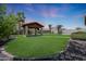 Backyard featuring a charming covered patio with a flat screen tv, set amongst a green lawn and manicured landscaping at 30308 W Whitton Ave, Buckeye, AZ 85396