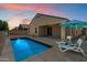 Backyard view of a private pool, covered patio and relaxing lounge chairs at twilight at 13612 W Desert Moon Way, Peoria, AZ 85383