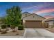 Single-story home featuring a well-manicured front yard, neutral tones, and a two-car garage, set against a beautiful sunset sky at 17573 W Via De Luna Dr, Surprise, AZ 85387
