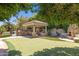 Backyard patio, covered outdoor kitchen, outdoor stone fireplace, putting green, and lush trees at 3731 E Halifax Cir, Mesa, AZ 85205