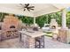 This luxurious outdoor kitchen boasts a pizza oven, a built-in grill and seating area with a fan above at 3731 E Halifax Cir, Mesa, AZ 85205