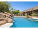 Backyard pool area showcasing rock waterfall feature, stone coping, black wrought iron fence and lush greenery at 3731 E Halifax Cir, Mesa, AZ 85205
