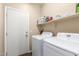 Functional laundry room with white washer and dryer, shelving, and convenient access door at 40089 W Bonneau St, Maricopa, AZ 85138