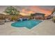 Scenic backyard featuring a pool with a waterfall feature, set against a vibrant sunset backdrop, with a covered dining area at 17815 W Straight Arrow Ln, Surprise, AZ 85387