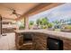 Covered outdoor kitchen area with stone bar, mini-fridge, grill, and seating, ideal for hosting gatherings at 550 W Powell Way, Chandler, AZ 85248